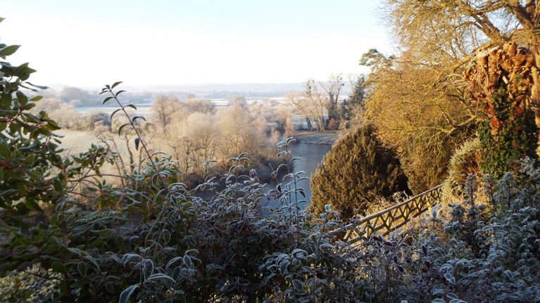 Foliage covered in frost bordering a view across the river wye and the frost fields in the background